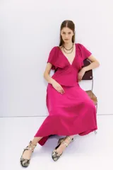 Vestido largo hasta el tobillo, color fucsia, con escote en V pronunciado y mangas cortas amplias con volados. Presenta un corte imperio con elástico en la cintura y espalda cuadrada.