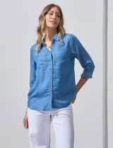 Camisa celeste de lyocell, con cuello a la base, escote en V y abertura central con botones. Tiene bolsillos aplicados en la parte delantera y mangas 3/4 regulables con presilla y botón.