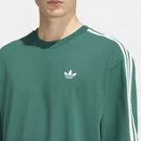 Remera Adidas de corte holgado en color verde, con cuello redondo, mangas cortas con las icónicas tres rayas blancas en los hombros y logo del trébol bordado en el pecho.