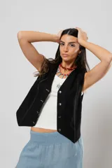 Chaleco negro con escote en V, sin mangas y cierre frontal con botones. Presenta pespuntes en color crudo en la parte delantera y logo bordado en la espalda.