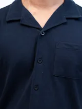 Camisa de manga corta color beige, confeccionada en tejido piqué de algodón, con cuello cubano y un bolsillo de parche en el pecho.