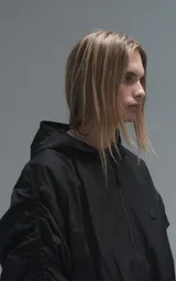 Campera rompevientos negra de calce oversize, confeccionada en microfibra técnica ligera con acabado semi-mate. Presenta capucha integrada, cierre frontal técnico y bolsillos tipo ojal. Destaca por su sistema de frunces elásticos regulables mediante tancas a lo largo de las mangas y el ruedo, permitiendo ajustar el volumen de la prenda.