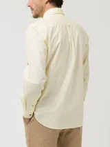 Camisa de manga larga RKF modelo Galiton, color amarillo, confeccionada en popelina 100% algodón orgánico. Cuenta con cuello camisero, botones de madera, un bolsillo frontal en el pecho con logo bordado y mangas ajustables.