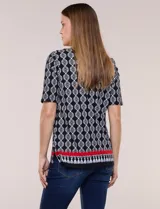 Remera de algodón con estampado geométrico en blanco y negro, de manga corta, con detalle de guarda roja y flecos en el ruedo.