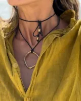 Collar con dije colgante de forma orgánica e irregular, acabado dorado, suspendido de un cordón negro de algodón natural.