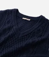 Chaleco de punto sin mangas con escote en V y aberturas laterales. Presenta una textura de tejido trenzado y un corte alargado, ideal para superposiciones.
