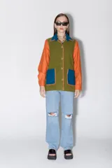 Camisa de paño confeccionada en lana, con diseño multicolor que combina paneles en verde oliva, naranja y azul. Presenta cuello clásico, cierre frontal con botones, bolsillos aplicados y detalles de bordados artesanales a mano en los bordes.