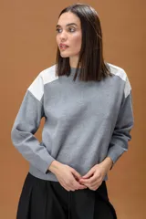 Sweater de punto color beige con cuello redondo y detalles de parches en cuero sintético blanco en los hombros. Presenta mangas largas con puños acanalados y un corte holgado.