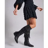 Bota texana alta de cuero vacuno color negro, con taco de madera foliado, punta fina y caña alta decorada con flecos hechos a mano. Cuenta con cierre lateral interno.