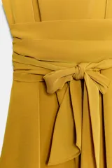 Vestido corto color mostaza con cuello fluido, manga sisa y hombreras marcadas. Presenta un detalle de lazada en la cintura y cierre de cremallera oculto en la espalda.