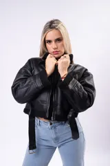 Campera tipo gamulán de cuero sintético marrón oscuro con interior y detalles de corderito sintético en cuello y puños. Presenta cierre frontal, bolsillos laterales con cierre y correas ajustables en el cuello.