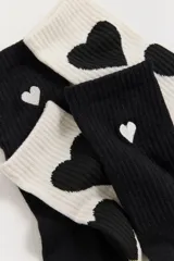 Pack de dos pares de medias de caña media, una en color negro con pequeño corazón blanco bordado y otra en color crema con estampado de corazones negros. Ambas cuentan con el logo de la marca bordado en el pie.
