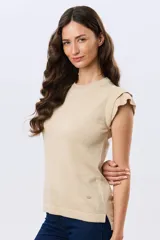 Remera tejida de algodón en color beige, de cuello redondo, sin mangas y con detalles de volados estructurados en los hombros.