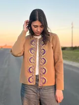 Chaqueta color beige tejida en lana con detalle de pasamanería bordada en el frente con motivos circulares en color violeta y dorado.