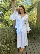 Camisa de lino azul marino con volados en cascada a lo largo del frente y en los puños de las mangas largas. Presenta un escote en V con un botón de nácar visible.