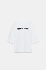 Remera oversize blanca de algodón con cuello redondo, mangas amplias por debajo del codo y estampado frontal con el texto "lost in Paris" en color negro.