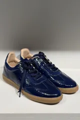 Championes de cuero vacuno con acabado brillante tipo charol, color azul marino, con cordones al tono y suela de goma color caramelo.