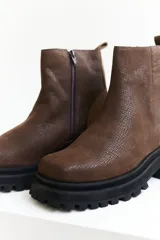 Bota corta de cuero color marrón con suela track negra y cierre lateral con cremallera.