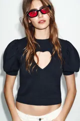Jersey de punto negro con cuello redondo y mangas cortas abullonadas. Presenta una abertura frontal en forma de corazón.