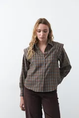 Camisa de manga larga con estampado de cuadros en tonos marrones, azules y amarillos. Presenta cuello clásico, cierre frontal con botones y hombros con estructura levemente marcada.