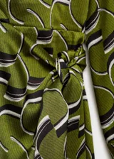 Vestido corto de tejido satinado con estampado geométrico en tonos verdes, negros y blancos. Presenta cuello camisero, mangas largas y un diseño cruzado que se ajusta en la cintura mediante un lazo lateral.