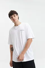 Remera blanca de manga corta con ajuste regular. Presenta un estampado en la espalda con un diseño floral lineal en gris, texto en inglés y el logo "BROOKSFIELD The vacation era" en azul.