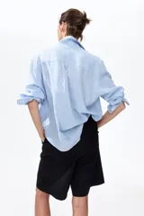 Camisa en tejido liviano de mezcla de lino y viscosa, a rayas celestes y blancas, con cuello, botones delanteros y bolsillo superior abierto. Modelo de manga larga con puños abotonados y bajo redondeado.