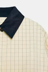 Chaqueta de corte recto confeccionada en algodón con estampado de cuadros. Presenta cuello solapa en color azul marino a contraste, cierre frontal con botones ocultos bajo solapa, bolsillos laterales y mangas largas con trabillas ajustables en los puños.