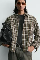 Camisa de corte relajado con estampado de cuadros en tonos marrones y blancos. Presenta cuello clásico, cierre frontal de botones, manga larga con puños abotonados y un bolsillo plastrón en el pecho.