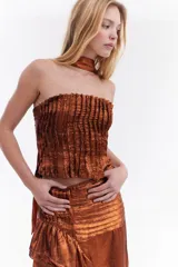 Top strapless de tela metálica con textura plisada, corte ajustado al cuerpo y diseño corto. Incluye una gargantilla a juego del mismo material.