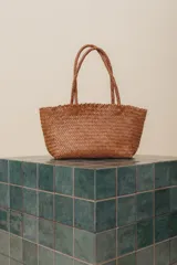 Bolso tipo tote de cuero vacuno, completamente trenzado a mano. El color es marrón oscuro, casi chocolate. Posee dos asas de hombro trenzadas.