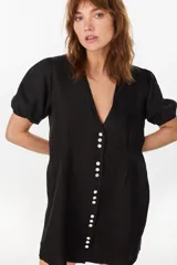 Vestido corto negro de lino italiano, con escote en V, mangas cortas abullonadas y cierre frontal de botones con cintura entallada y tablas.