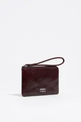 Monedero de piel color marrón rojizo con acabado brillante, estructura rígida y cierre de cremallera con tirador de tejido. Presenta logo metálico de Bimba y Lola en el frente y bolsillo interior.