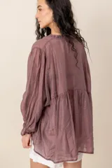 Blusa de seda gris con mangas largas abullonadas y puños con volados, escote en V con cuello fruncido y botones frontales.
