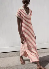 Vestido largo de punto fino con diseño a rayas horizontales rojas sobre fondo beige, de corte recto, manga corta y cuello polo en V.