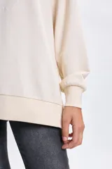 Buzo deportivo de corte oversize en color crudo, con cuello redondo y mangas largas. Presenta un diseño bordado en el frente con la inscripción Saint Tropez y un motivo floral central.