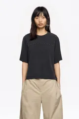 Camiseta de manga corta, corte boxy y escote redondo, color negro, con tachuelas metálicas decorativas en la parte delantera a la altura de los hombros y el pecho.