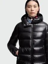 Campera puffer de corte largo con acabado brillante, cierre frontal, capucha integrada y bolsillos laterales con cierre. Presenta el logo de la marca en la manga izquierda.