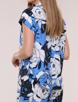 Camisa de manga corta confeccionada en rayón y poliéster, con estampado floral en tonos azules, negros y blancos, cuello camisero clásico y cierre frontal de botones.