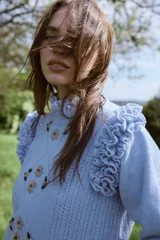 Sweater de punto color celeste, con diseño de rombos calados y bordados florales artesanales en el frente. Presenta volados decorativos en los hombros y cuello redondo.