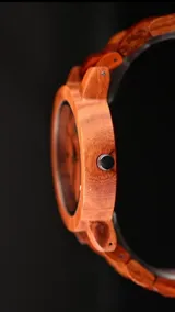 Reloj de pulsera con caja, esfera y malla de madera de sándalo rojo, con marcadores y manecillas negras. Presenta un diseño circular con corona lateral.