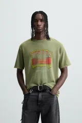 Camiseta de punto de algodón con corte relaxed fit, cuello redondo y manga corta. Color verde oliva con efecto lavado y estampado frontal con diseño gráfico en tonos rojo y amarillo.