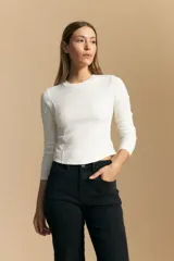 Remera blanca de manga larga con tejido acanalado, cuello redondo y corte ajustado al cuerpo. Presenta costuras verticales que definen la silueta.