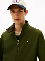 Campera tipo Harrington de Tommy Hilfiger en color verde militar, con cuello alto, cierre frontal de cremallera y bolsillos laterales. Cuenta con elásticos en puños y dobladillo, y el logo bordado en el pecho.