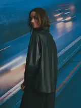 Sobrecamisa de cuero sintético en color negro, con cierre frontal de botones metálicos a presión, cuello clásico y un bolsillo frontal en el pecho.