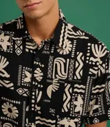 Camisa de hombre marca Blue Steel, modelo relaxed, confeccionada en tricolina de algodón. Presenta manga corta, cuello inglés, cierre frontal con botones y un bolsillo de parche. El diseño destaca por su estampado abstracto de verano con motivos de palmeras en color beige sobre fondo negro.