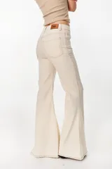 Jeans acampanados de tiro alto color beige, confeccionados en denim con costuras contrastantes y terminación deshilachada en el bajo.
