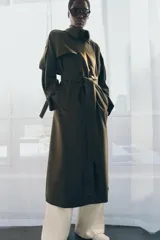 Trench oversize de Zara Woman Collection, color verde militar, con cuello solapa, cierre frontal cruzado con botones y cinturón ajustable del mismo tejido. Presenta mangas largas con trabillas ajustables y bolsillos delanteros.