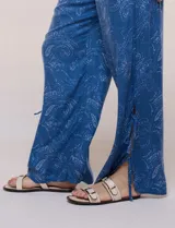 Pantalón palazzo de rayón color azul con estampado paisley blanco, corte amplio, tiro medio-alto con pretina elastizada y aberturas laterales en el puño regulables con lazos.