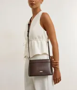 Bolsa bandolera de estructura firme en color marrón oscuro, con cierre de cremallera metálica y correa larga ajustable con hebilla.